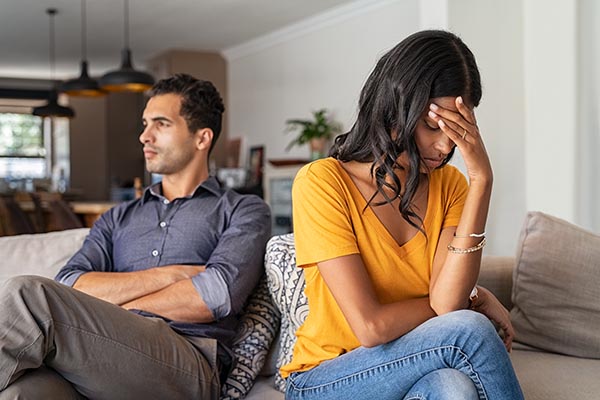 Middle eastern young couple sitting on couch after a fight. Sad indian woman sitting with hand on head after quarrel with boyfriend at home. Angry couple ignoring each other, relationship troubles.